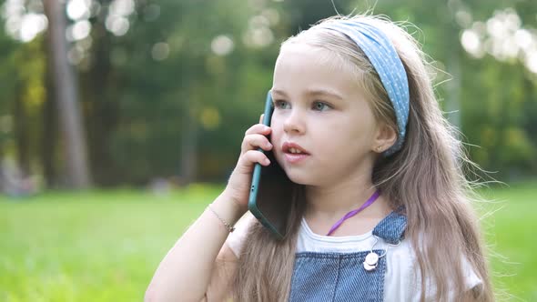 Pretty Little Child Girl Having Conversation on Her Mobile Phone in Summer Park