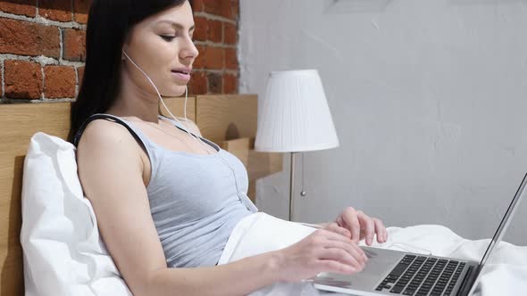 Relaxing Woman Enjoying Listening Music on Laptop in Bed