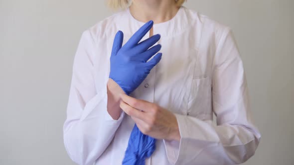 A Female Doctor Surgeon in White Uniform Puts on Blue Gloves