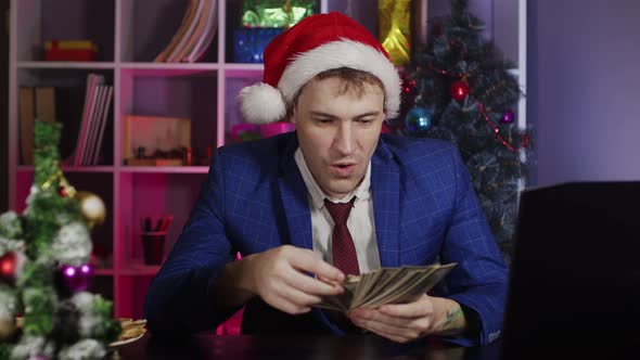 Happy Businessman in Santa Hat with Money in Office