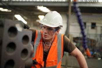  Worker Wearing Safety Uniform, Goggles and Hard Hat. In the Background Unfocused Large Industrial Factory