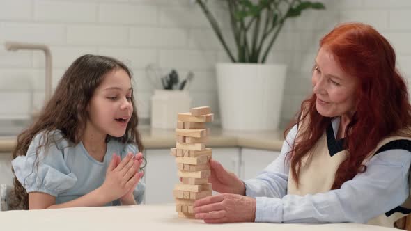 Grandmother and Granddaughter are Playing a Board Game at Home Removing Wooden Blocks From the Tower