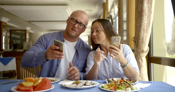 An Adult Couple Laughs While Watching Funny Videos on a Smartphone or Mobile Phone While Sitting in