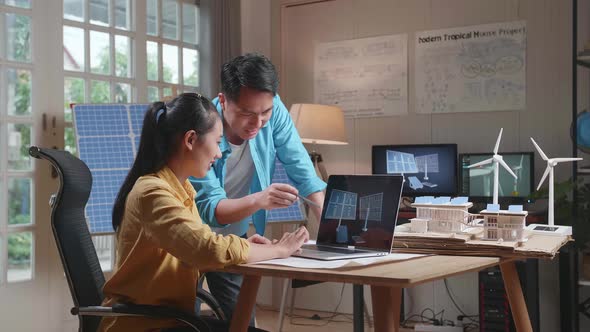 Man And Woman Discuss About Solar Cell On Laptop Next To The Model Of A Small House With Solar Panel