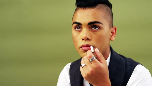 Androgynous man posing with cigarette against green background