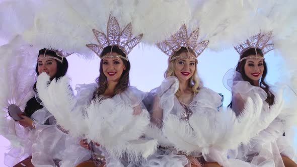 Adorable Women in White Snow Queen Costumes and Feather Headdresses Blow Glitter and Have Fun