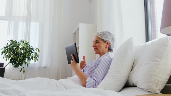 Old Woman with Tablet Pc Having Video Call in Bed