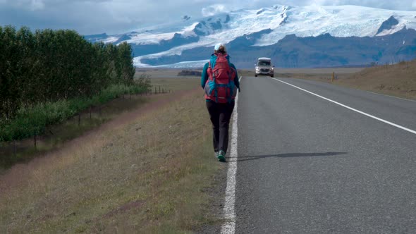 Woman Traveler with a Backpack Is on an Asphalt Road