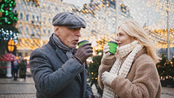 Close Up of Happy Senior Man and Woman Drinking Hot Coffee Outdoors Enjoying City Christmas Fair