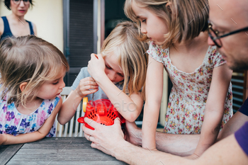 Three beautiful female children outdoor terrace adjusting bubble soap machine helped by their father