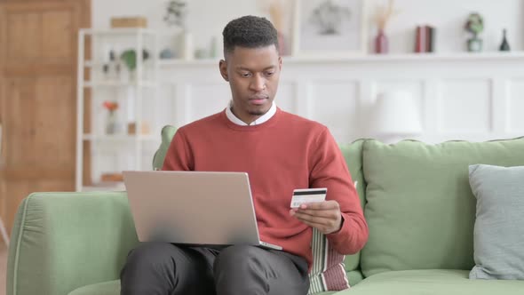 African Man making Online Payment on Laptop on Sofa