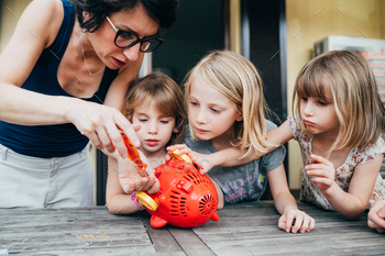 Three beautiful female children outdoor terrace adjusting bubble soap machine