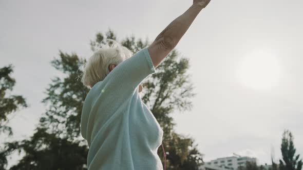 Senior Retired Woman Enjoying Freedom of Retirement. Outstretched Hands in the Park, Low Angle Shot