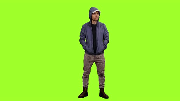 Hooded Man Stands with Hands in Pockets on Green Background