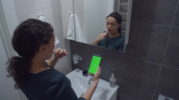 Black Woman Looking at Smartphone with Chroma Key While Brushing Teeth