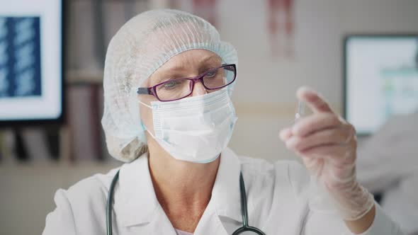 Medical Worker in Safety Gloves Mask and Cap Holding Ampoule with Vaccine