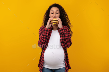 er Eating Junk Food Posing Over Yellow Orange Studio Background. Woman Enjoying Big Hamburger. Unhealthy Nutrition And Binge Eating Habit Concept