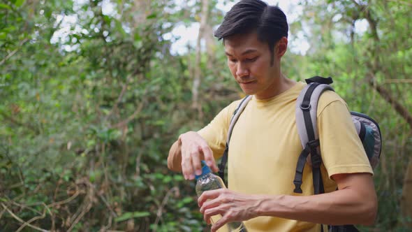 Young Asian man backpacker traveler feel tired and stop drinking fresh water while travel in forest.