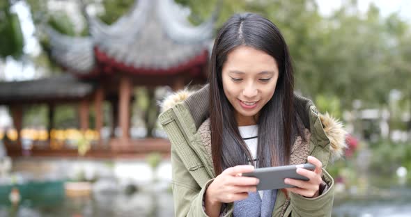 Woman concentrate using cellphone and standing at outdoor Chinese garden 