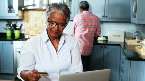 Senior woman doing online shopping on laptop in kitchen at home