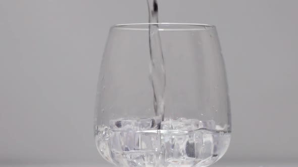 Pouring Water Into Glass with Ice on White Stone Background