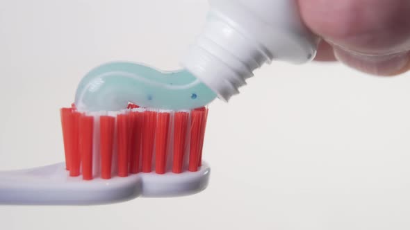 A hand squeezes a blue toothpaste from a tube onto a white plastic toothbrush 