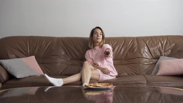 Bored Young Woman Sitting on the Brown Leather Sofa at Home Watching TV
