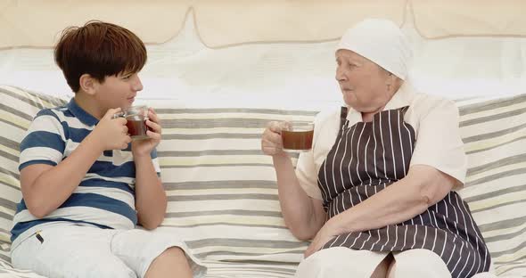 A Teenager and His Grandmother are Drinking Tea While Sitting on a Garden Swing