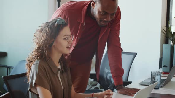 Two Multiethnic Male and Female Coworkers Discussing Project on Laptop