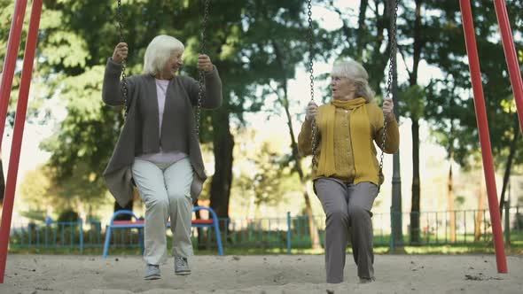 Two Senior Ladies Enjoying Ride on Swings in Park, Elderly Friends, Retirement