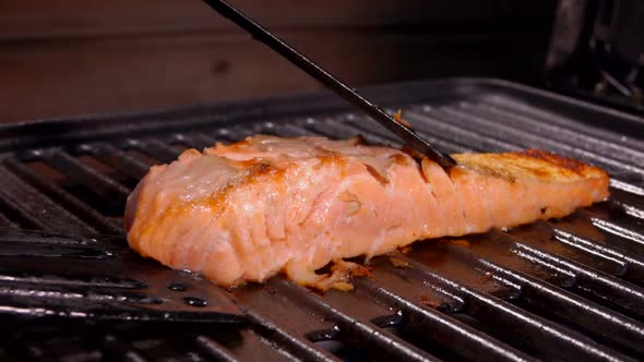 Cook is Flipping a Piece of Raw Salmon Fillet Steak with a Black Kitchen Spatula