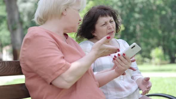 Side View of Blond Modern Female Retiree Showing Social Media To Friend and Brunette Arrogant Woman