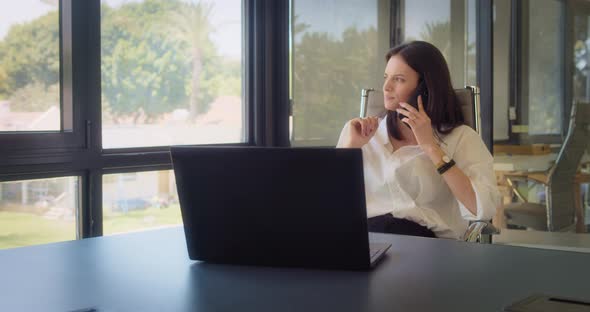 A businesswoman in white blouse talking on the phone, while working at the office.