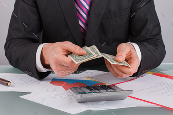 t table. Businessman or banker holding money while working with financial documents at office.