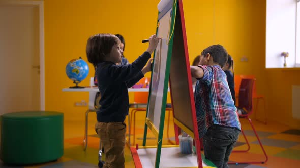 Creative Multicultural Boys Drawing on Easel Board