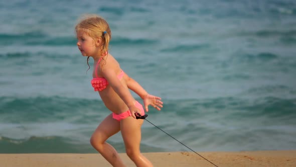 Little Cute Girl in Pink Swimsuits is Playing with a Swimming Board on the Beach