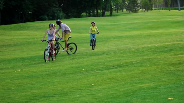 Four Cheerful Students Cycling on Green Lawn