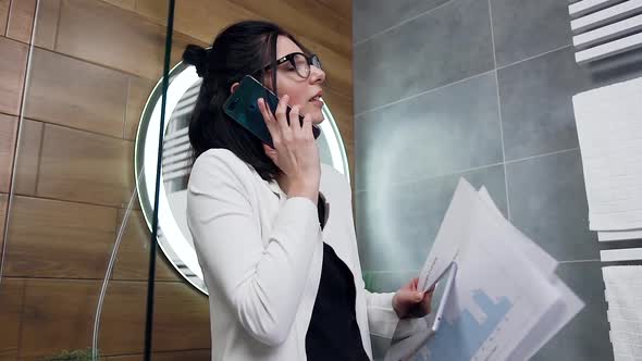 Business Woman Which Standing in the Bathroom and Talking on Her Smartphone