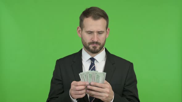 Young Businessman Counting and Offering Money Against Chroma Key