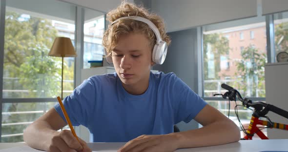 Caucasian Teen Boy in Headphones Writing Down Info During Online Lesson on Laptop at Home