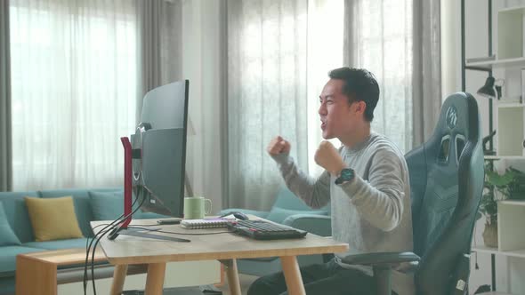 Asian Man Looking At Desktop Computer Screen And Winning The Project While Working At Home