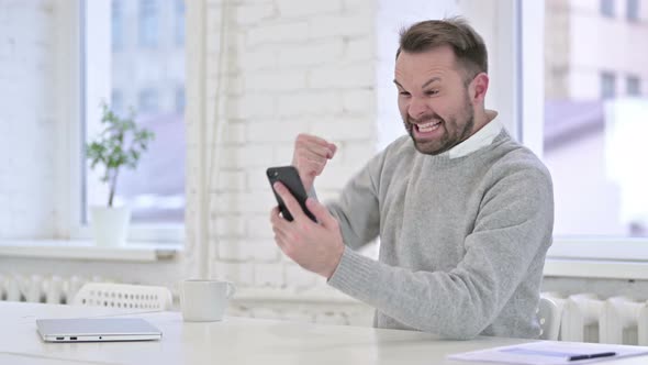 Excited Man Celebrating Success on Smartphone at Work