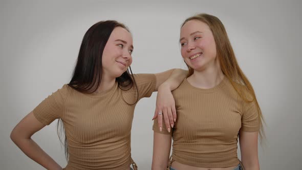 Relaxed Confident Twin Sisters Posing at Grey Background Looking at Camera Laughing