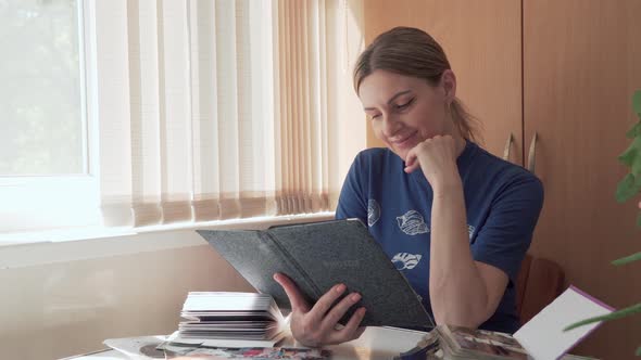 Young Woman Looks at Photos From Family Photo Album Recalling Past Time