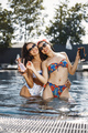 Two female friends in a swimwears relaxing with a cocktails in a swimming pool - PhotoDune Item for Sale