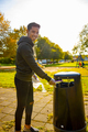 Smiling young volunteer putting straws in garbage bin at park - PhotoDune Item for Sale