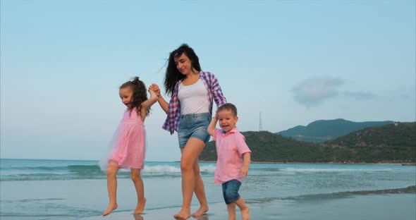 Young Family, Mother and Children Are Walking Along the Coast. Happy Family Walking on Sea Coast.