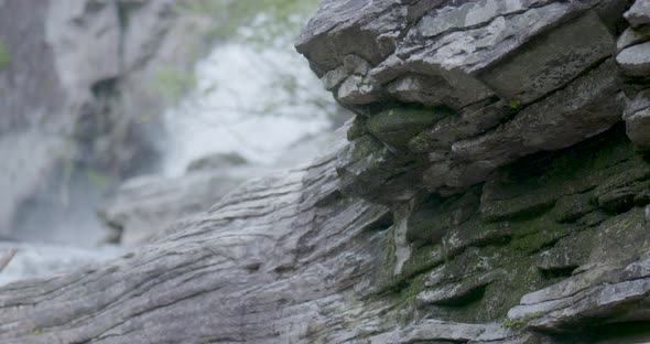 mossy rock dripping water while rushing waterfall behind rock