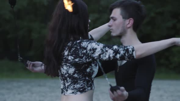 Young Slim Man in Black Clothes and Attractive Woman Perform Show with Flame Outdoors