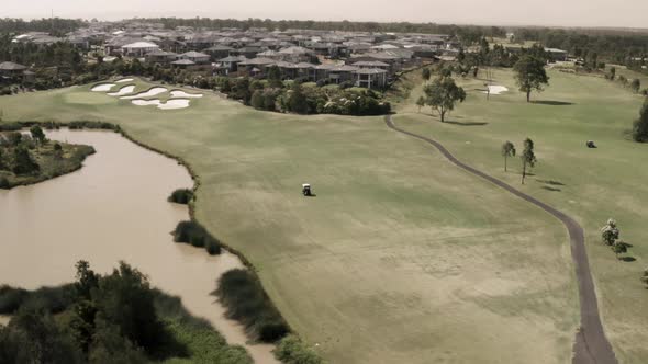 Aerial video following a golf cart drive up the fairway on a long hole at a golf course